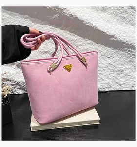 Detail of pink suede tote bag featuring a gold triangle logo and cylindrical handles