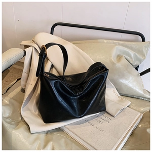 Detail of black large tote bag with adjustable gold buckle strap and zipper on leather sofa