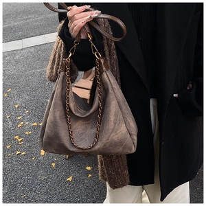 Close-up of retro suede hobo bag with fashion label and chain strap in autumn street
