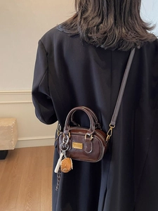 Deep brown mini Boston bag with gold brand plate and baseball charm on a cross-body strap
