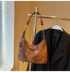 Detail of dark brown hobo bag featuring amber bead shoulder strap and metallic logo