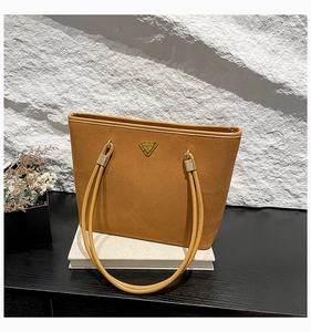 Detail of a brown suede tote bag featuring a golden triangle logo and metallic hardware