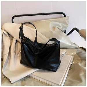 Detail of black glossy leather hobo bag with gold buckle on a white book prop