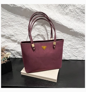 Detail of burgundy suede tote bag featuring a gold triangle metal plate and slim straps