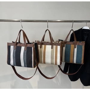 Three striped woven tote bags in various colors displayed on a rack with leather straps