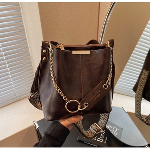 Détail du sac seau en cuir marron vintage avec bandoulière tissée et finitions dorées