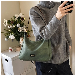Detail of dark green suede tote with fashion label and gold chain shoulder strap