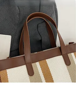 Detailed close-up of striped canvas tote bag with premium brown leather handles and stitching