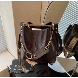 Détail du sac seau marron vintage en cuir brillant avec chaîne dorée et bandoulière tissée