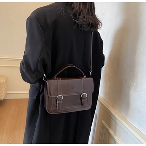 Detail view of a vintage dark brown square bag with metal buckles on a black coat