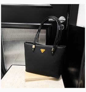 Detail of minimalist black tote bag with triangle metal logo and slim shoulder straps