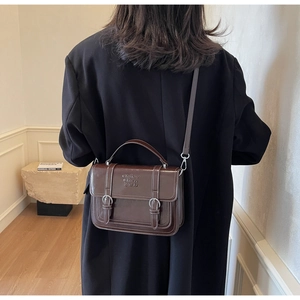 Detail showing the dark brown glossy leather handbag with crossbody strap and metal buckles