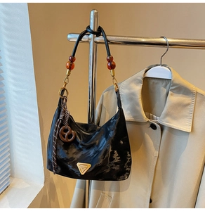Detail of black nylon shoulder bag with golden triangle logo and pretzel charm accessory