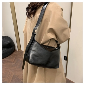 Detail of a black glossy crossbody bag with adjustable strap on a long khaki coat