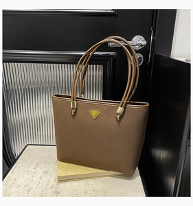 Detail shot of a brown suede tote bag featuring a triangle gold logo and long handles