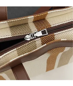 Detail of polished silver zipper on striped canvas tote bag with brown leather trim