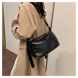 Macro shot of minimalist black matte leather crossbody bag worn with a beige trench coat