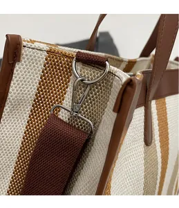 Detail of silver metal swivel hook and brown strap on striped canvas tote bag