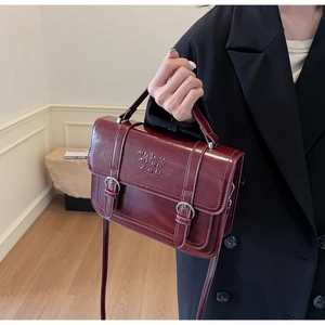 Detail of burgundy patent leather handbag with embossed lettering and metal buckles