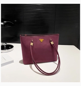 Detail of burgundy suede tote bag with golden triangle hardware and long shoulder straps