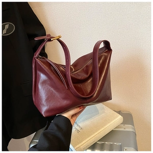 Detail of burgundy leather tote bag with gold hardware held against a business suit