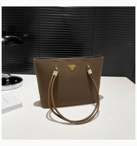 Close-up of brown suede tote bag featuring a gold triangle logo and metallic buckle details