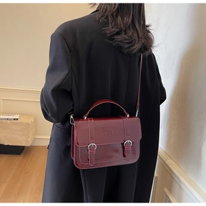 Detail view of a vintage burgundy leather crossbody bag worn by a model in a black suit