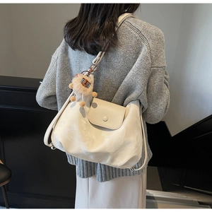 Detailansicht der cremeweißen Oversize-Hobo-Tasche mit braunem Plüsch-Löwenanhänger