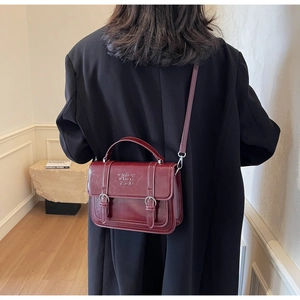 Close-up of a burgundy glossy leather crossbody bag worn with a black winter coat