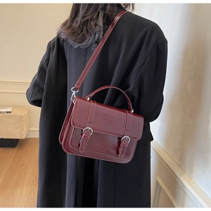 Detail of burgundy patent leather handbag featuring dual straps and embossed logo design