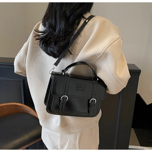 Detail of black patent leather crossbody bag with dual straps and engraved logo on cover