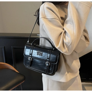 Black glossy crossbody bag with double buckle straps worn with a casual beige outfit