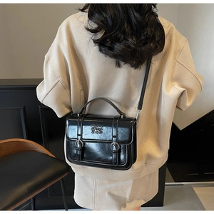 Detail of a black glossy crossbody bag with embossed letters shown on a model