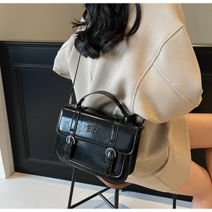 Detail of black glossy leather crossbody bag with silver buckles and embossed text