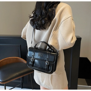 Detail of black vintage satchel showing elegant embossed text and dual buckle straps