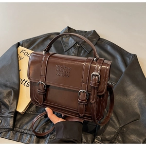 Detailed view of dark brown leather handbag with double buckles and embossed logo