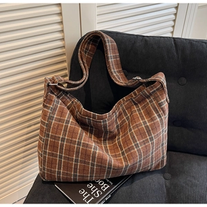 Detailed texture of brown plaid tote bag with metal buckle on a cozy sofa setting
