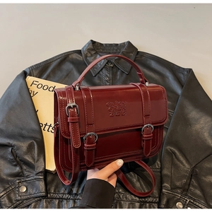 Close-up of burgundy glossy leather handbag with double buckle straps and embossed logo