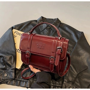 Detail of retro dark burgundy messenger bag with top handle and decorative buckle straps