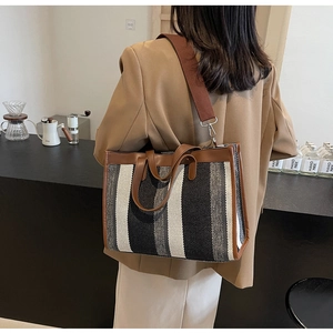 Detail of striped canvas tote bag with brown leather trim and wide canvas shoulder strap