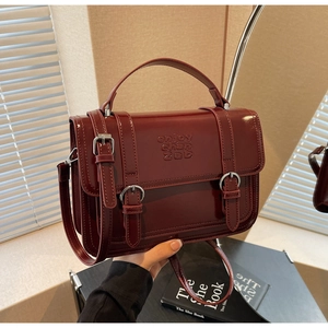 Close-up of deep red vintage messenger bag with silver buckles and stamped lettering