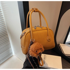 Detailed close-up of ginger yellow litchi leather bowling bag with cute plush bear charm