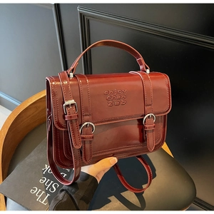 Close-up of a burgundy patent leather handbag featuring embossed lettering and silver buckles