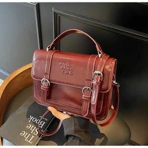 Detailed close-up of glossy burgundy leather handbag with dual strap buckles and embossed logo