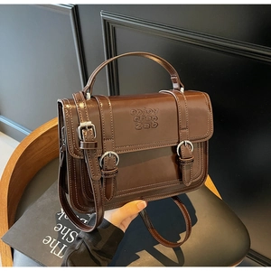 Detail of vintage brown leather handbag with embossed text and metallic buckle closure