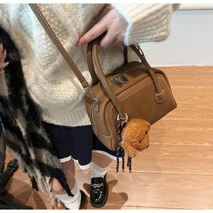 Close-up of brown pebbled leather bowling bag with white stitching and plush dog charm