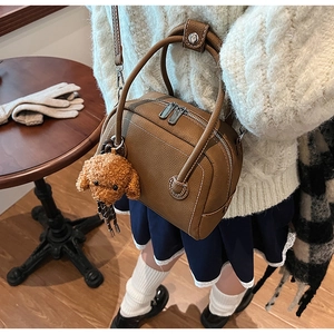Detail of brown litchi leather bowling bag featuring a cute teddy plush charm