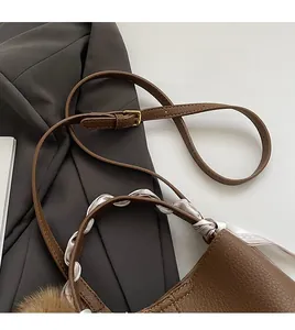 Close-up of brown textured leather bucket bag with silk scarf and plush charm detail