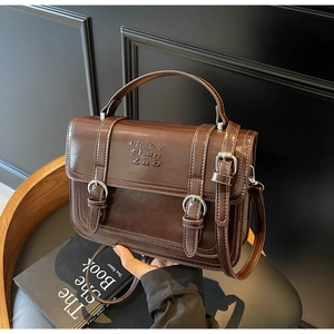 Detailed shot of dark brown glossy leather handbag featuring embossed brand lettering and dual straps
