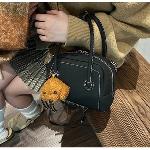 Detail of black shell bag with white stitching and brown plush teddy bear charm